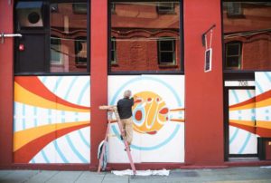 Image of artist on ladder painting mural on downtown Tacoma business